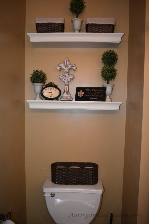 Two white shelves over a toilet holding baskets showing organizing ideas for your home. 