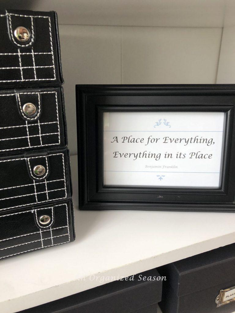 The motto "A place for everything, Everything in it's place" inside a black picture frame on the bookshelf.