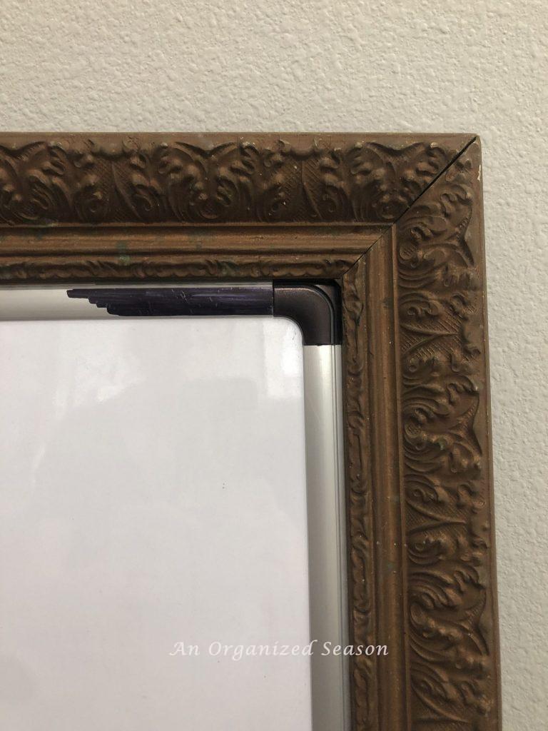 Gold frame with silver edge being covered with black sharpie showing how to update a whiteboard to match your decor.