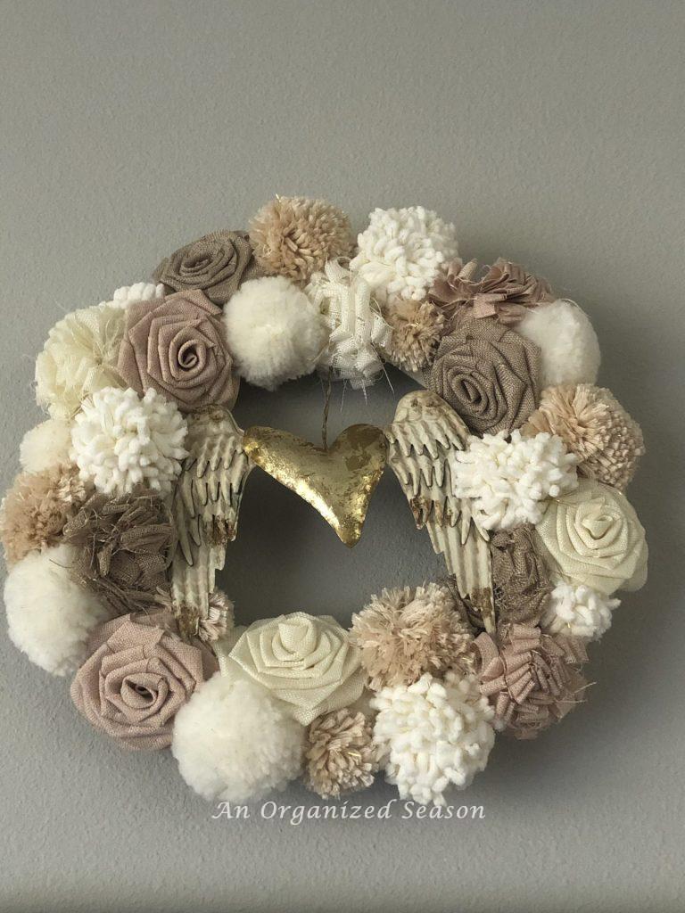 A pompom wreath that I embellished with angel wings attached by a gold heart is perfect idea for decorating for Valentines day.