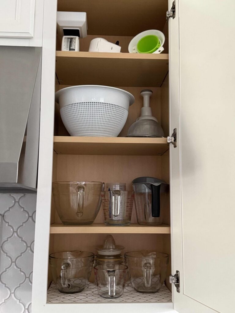 Kitchen cabinet with organized measuring cups, bowls, and strainers. 