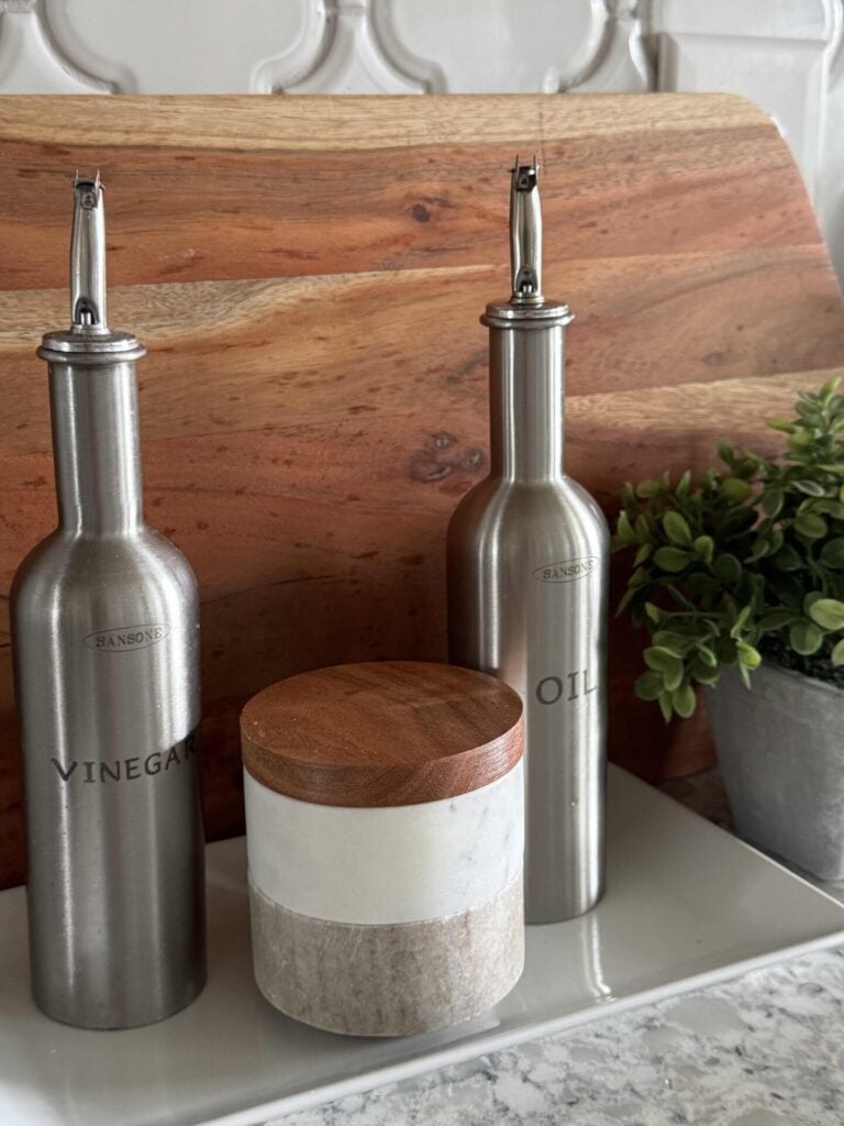White tray holding silver oil and vinegar bottles and a stacked salt and pepper canister. 