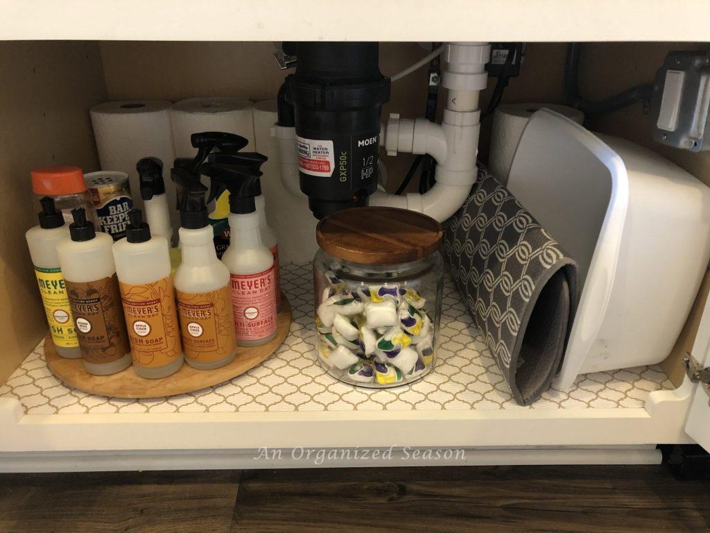 a lazy Susan with cleaning products, a jar with dishwashing tabs, cleaning tub and drying pad that show how I organized my kitchen using zones.  