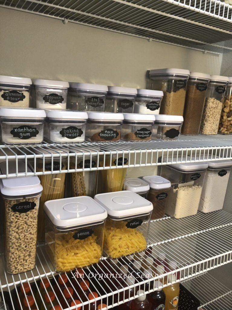 Two shelves in my pantry holding OXO storage containers filled with baking supplies, pasta, and cereal to show how to organize your kitchen pantry