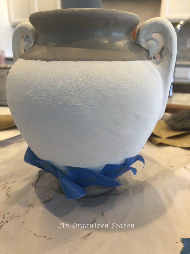 A vase with painters tape showing how to update an old decor item by painting it.
