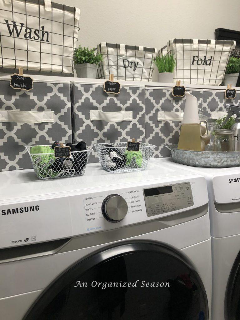 Wire baskets and cloth bins sitting above the washer and dryer to show how to organize your laundry room.