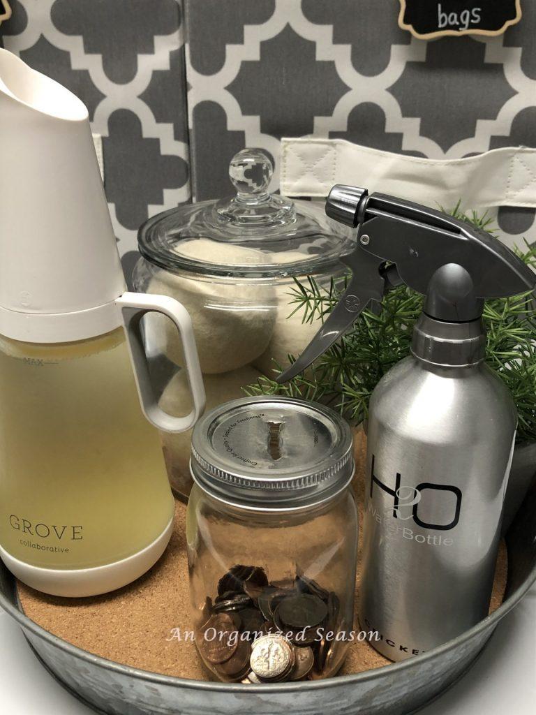 An example of how you can organize your laundry room by putting your detergent, dryer balls, a spray bottle and coin jar on a tray on top of the washer.