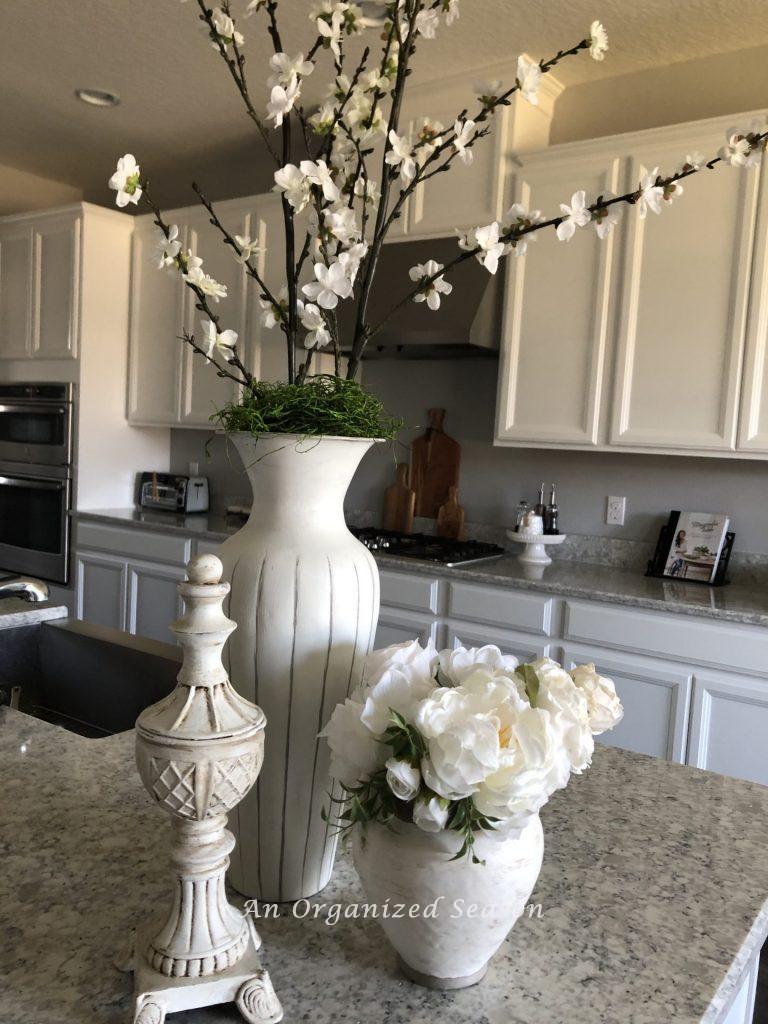 I did an update on three old home decor items by painting them white. There is a statue and two vases filled with flowers on a kitchen counter. 