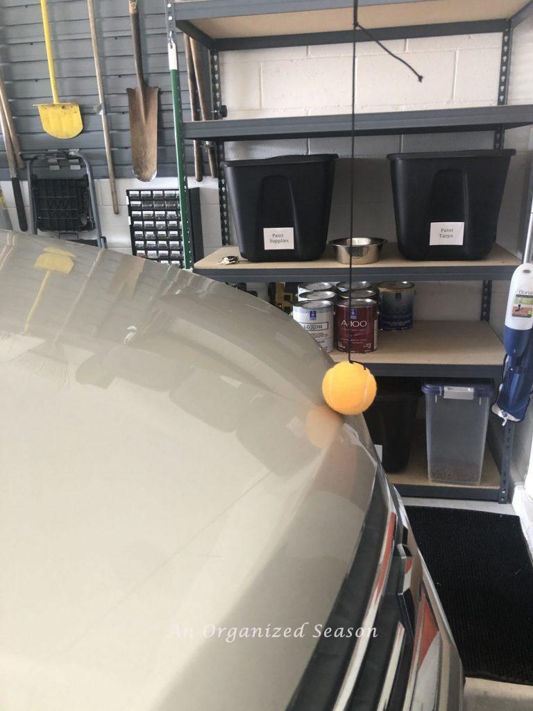 Car parked in garage touching an orange tennis ball hanging from the ceiling.  Park assist is one of the steps to garage organization.