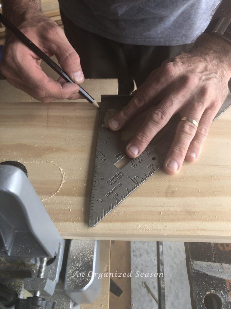 Marking a line on the wood showing step two of how to build a personalized coat rack.