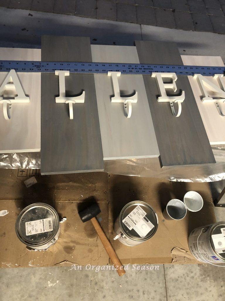 A long metal ruler aligning letter coat hangers that will be screwed onto the boards showing how to build a personalized coat rack.