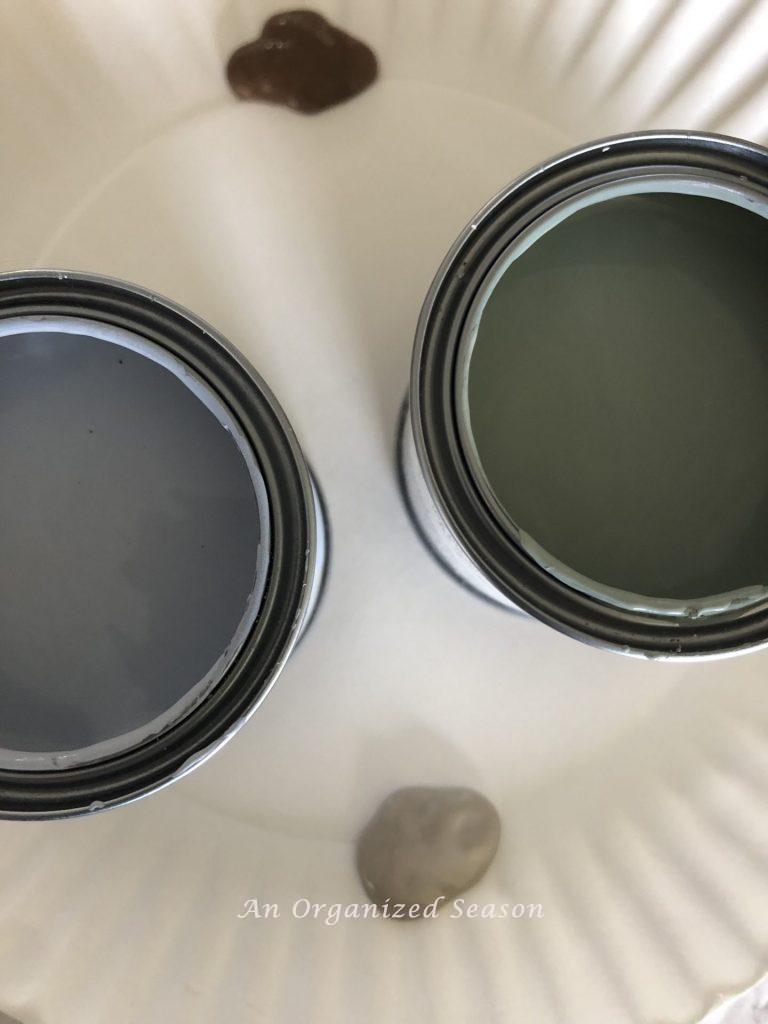 Two cans of paint showing the colors Louie Blue and Duck Egg blue.  Two blobs of acrylic paint called Coffee Bean and Barn Wood.  I will use these colors to make realistic eggs to add to my Spring decor.
