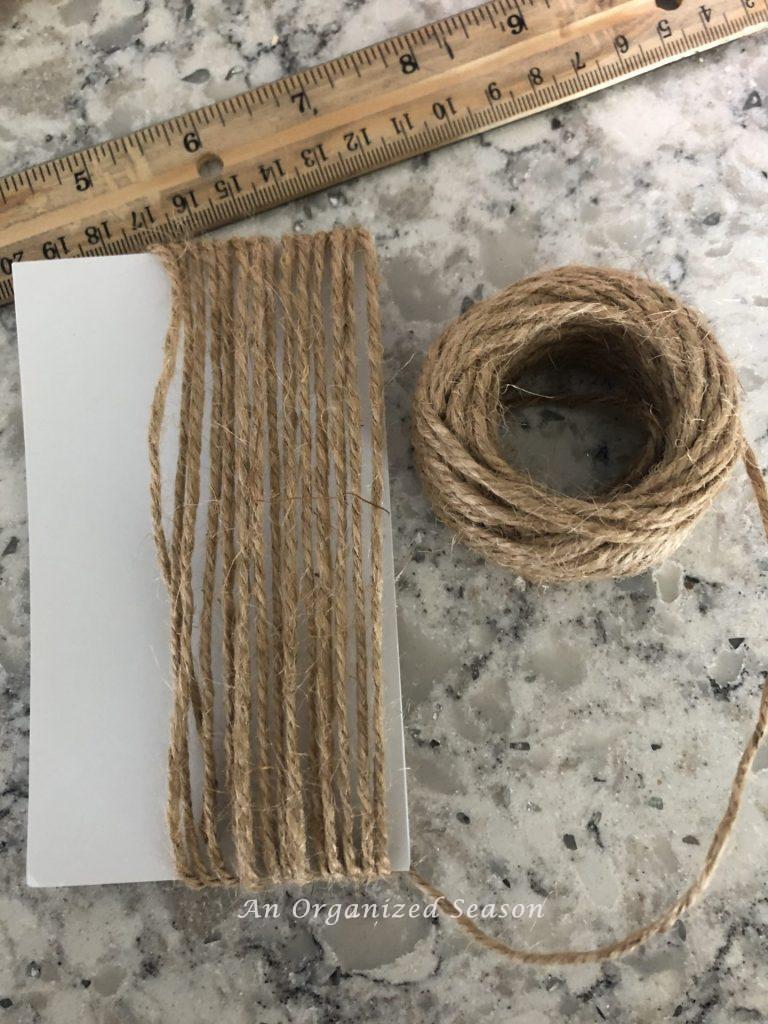 Jute twine wrapped around an index card fifteen times showing how to make a wood bead garland with tassels. 