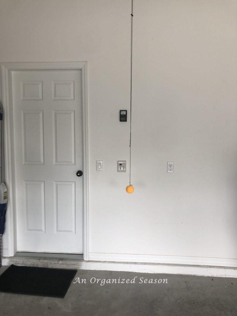 An orange tennis ball hung from the garage ceiling by a black cord to assist in parking the car.  Part of steps to garage organization. 