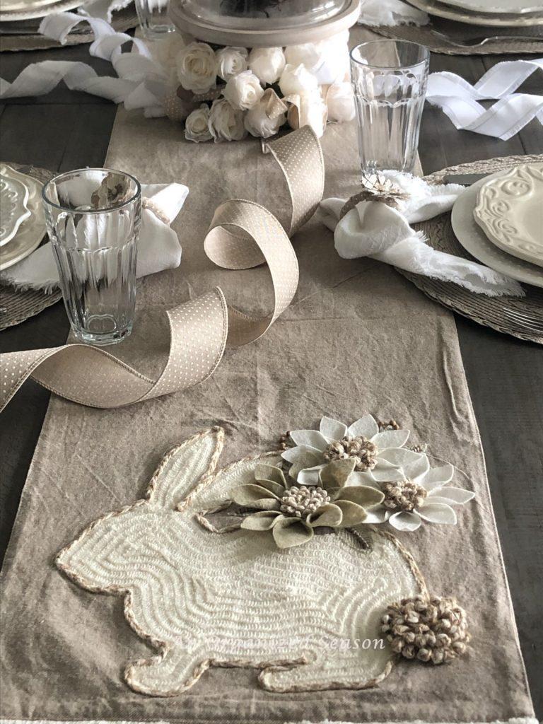 Dining table with a beige runner with a bunny and flowers embroidered on the end. Showing first tip for creating a simple Easter tablescape. 