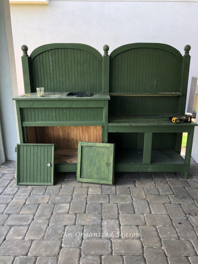 Wooden potting bench painted green with doors removed.  The before picture for how to give new life to an old potting bench.