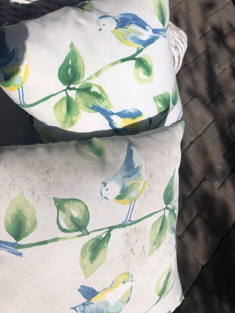 An outdoor pillow with mildew stains next to an identical pillow with the mildew cleaned off it.  Example of step three for how to enjoy your porch this Spring.