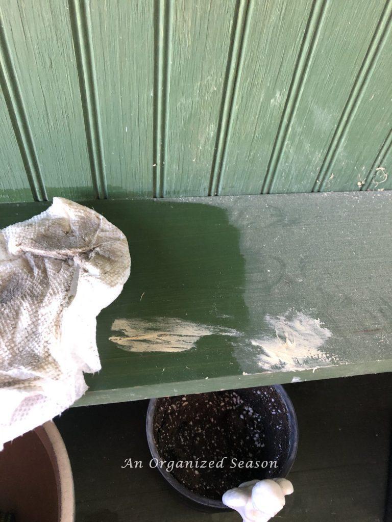 Green potting bench covered in pollen.  A wet cloth has removed some of the pollen.  Step one for how to give new life to an old potting bench.