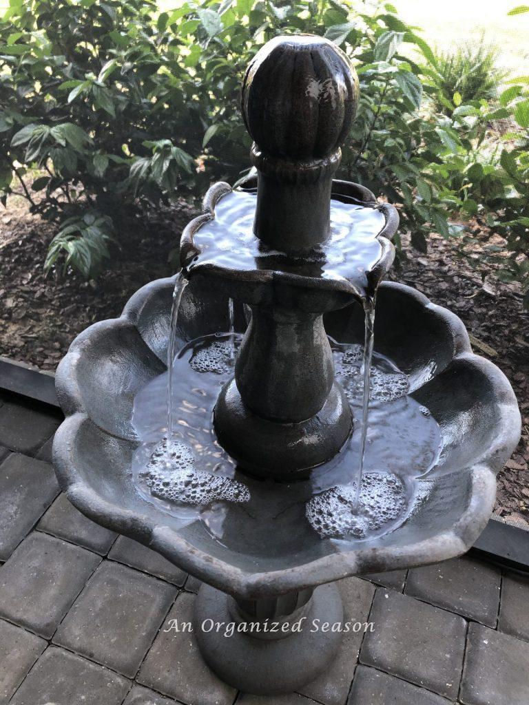 A concrete, two-tiered water fountain sitting on a paved porch.  Provides beauty and nice sounds to help you enjoy your porch this Spring.