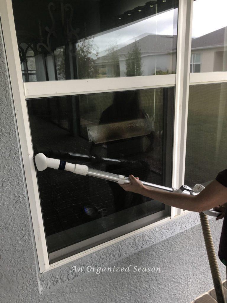 A woman vacuuming dust and pollen off a window screen. Step three for how to enjoy your porch this Spring. 