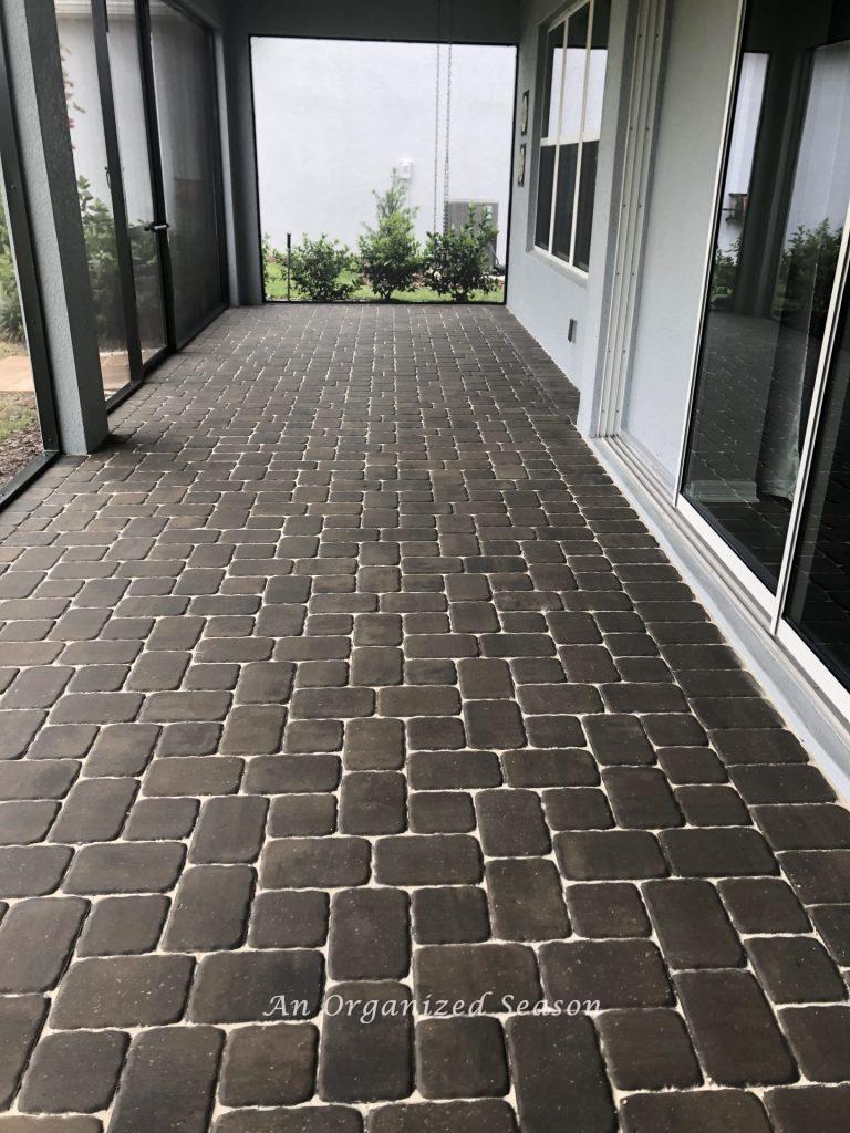 An empty screened in back porch with pavers that have just been sealed.  An example of step three for how to enjoy your porch this Spring.