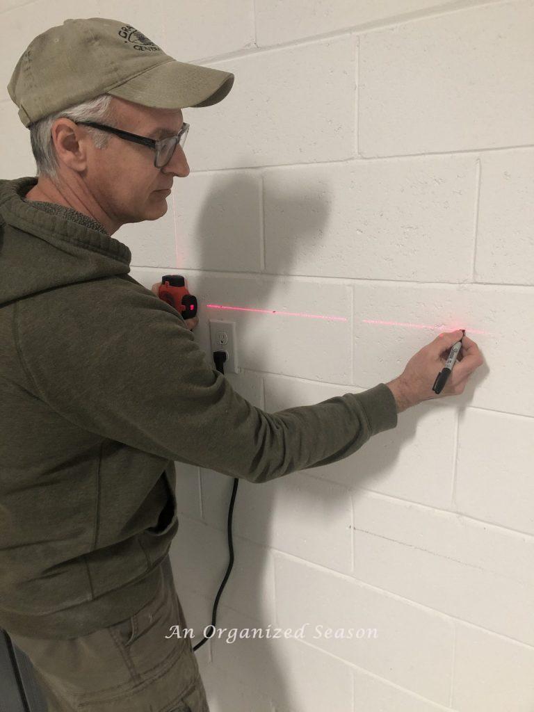 A man using a level to mark a spot on a garage wall. Step three for how to install a Flow Wall system. 