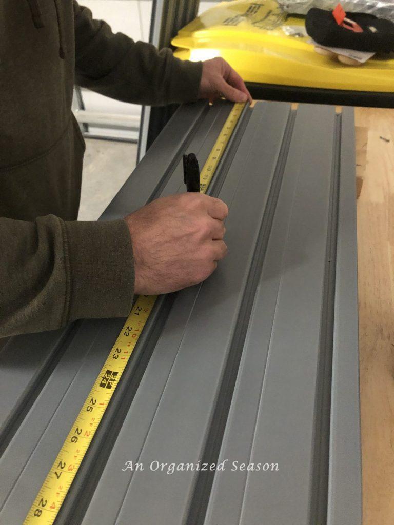 A measuring tape over a Flow Wall panel and someone's hand marking a spot to drill hole. Step one for how to install a Flow Wall System.