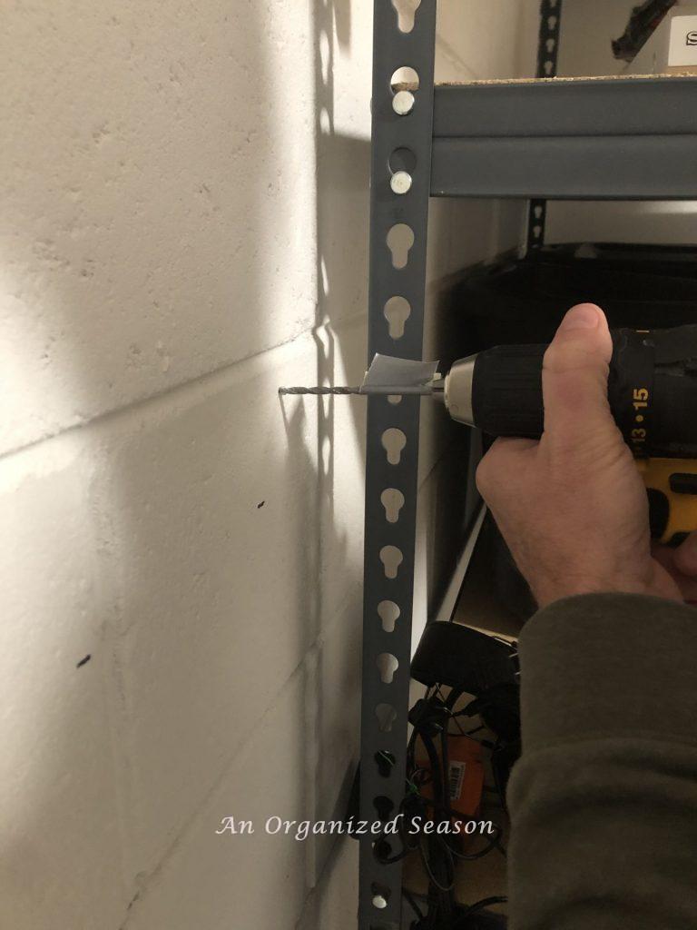 A man drilling a hole into a garage wall showing step five for how to install a Flow Wall system.