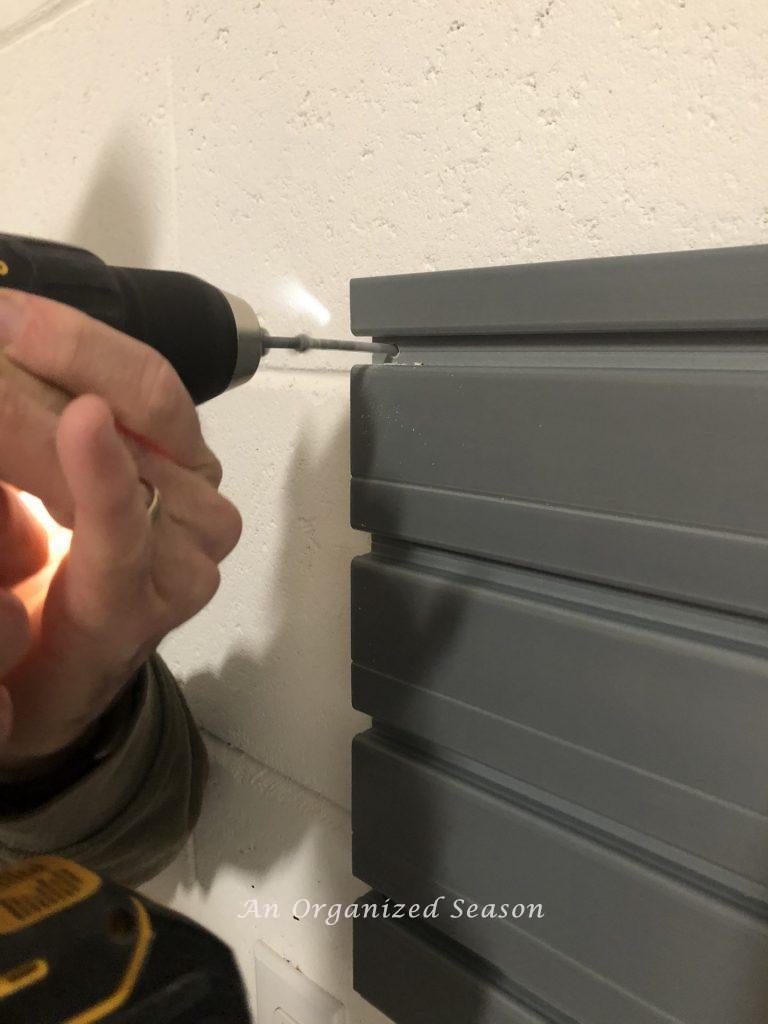 A man inserting a screw to hold the panel on the wall. Step six for how to install a Flow Wall system.