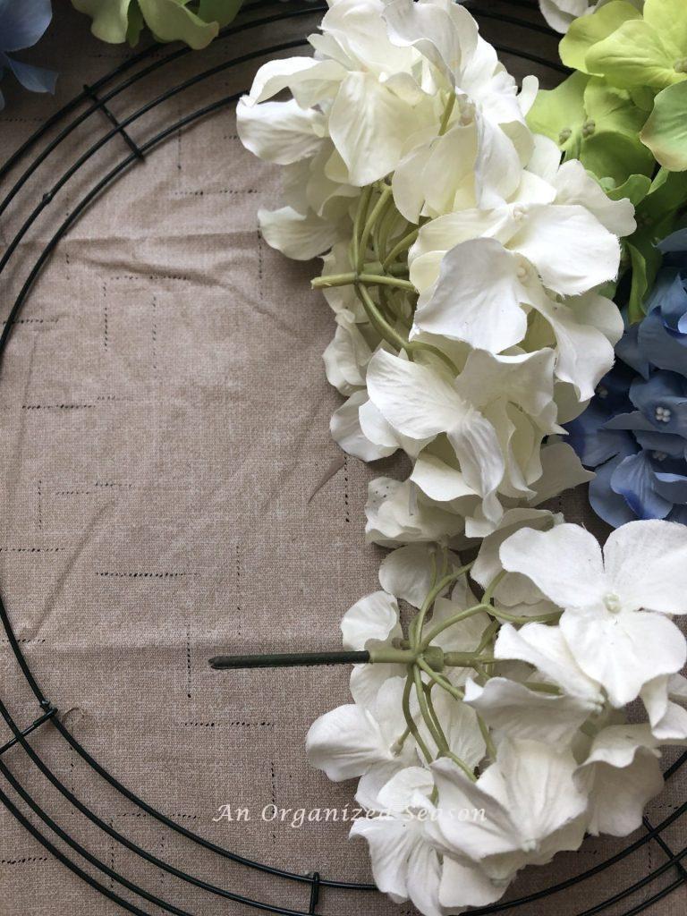 Two white hydrangea blooms. One has a stem and one does not. Example of step two for how to make a spring wreath using hydrangea.