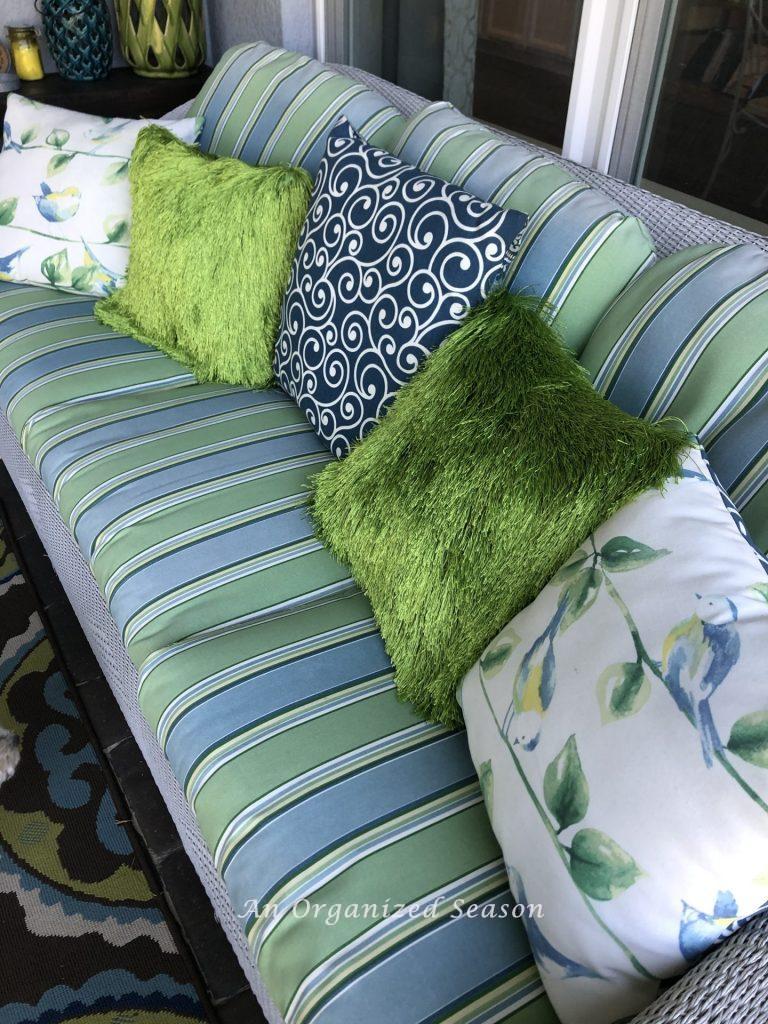 Five pillows on a white wicker couch.  Comfy seating to allow you to enjoy your porch this Spring.