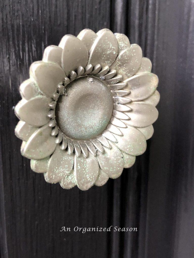 Up close picture of the cabinet hardware on a potting bench.  A silver sun flower head that is starting to get a bit of patina on it.  Showing an example of how to give new life to an old potting bench! 