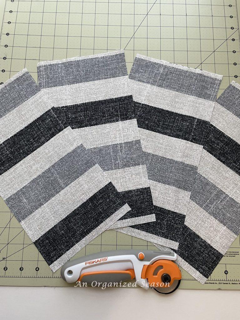 Four pieces of fabric that have been cut, laying on a cutting mat beside a rotary blade cutter. Showing step fifteen for steps to transform a worn out cornhole set. 