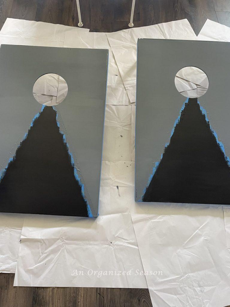 Two gray cornhole boards with a new black painted triangle.  Step 8 for steps to transform a worn out cornhole set.  