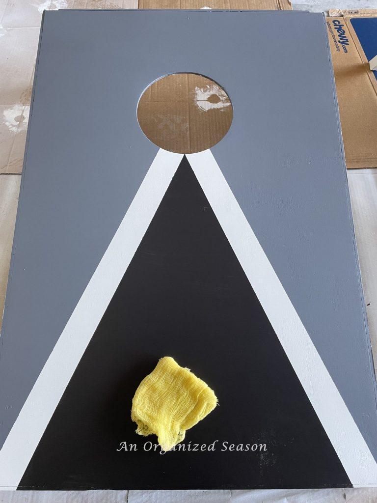 A newly painted cornhole set with a tack cloth on top of it.  Showing step ten for steps to transform a worn out cornhole set. 