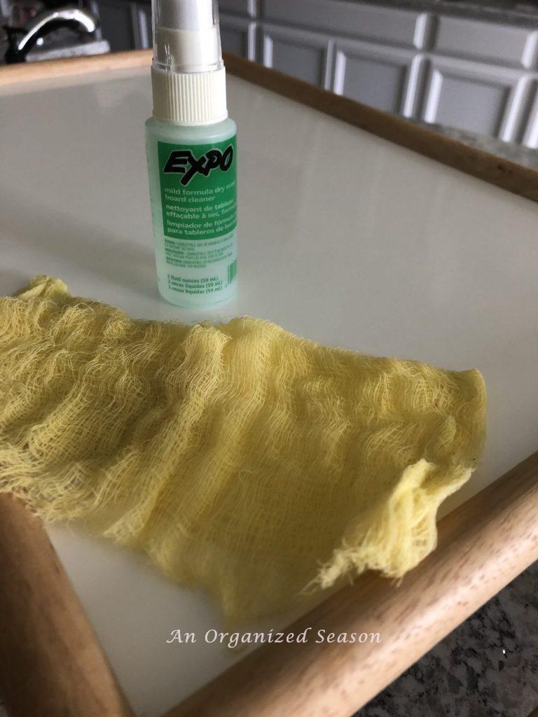 A bed tray with a bottle of dry erase cleaner and a tack cloth sitting on it.  Showing items needed for step one of how to makeover a breakfast in bed tray.