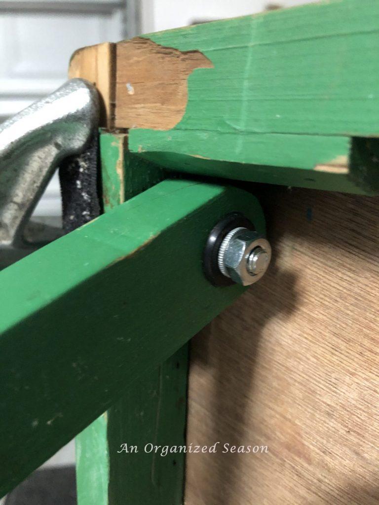 The leg of a cornhole board with new screws to hold it on.  Showing step three for steps to transform a worn out cornhole set.