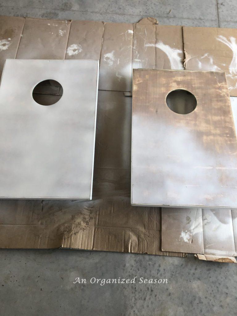 A cornhole board with primer and a second board that is partially primed. Showing step four for steps to transform a worn out cornhole set. 