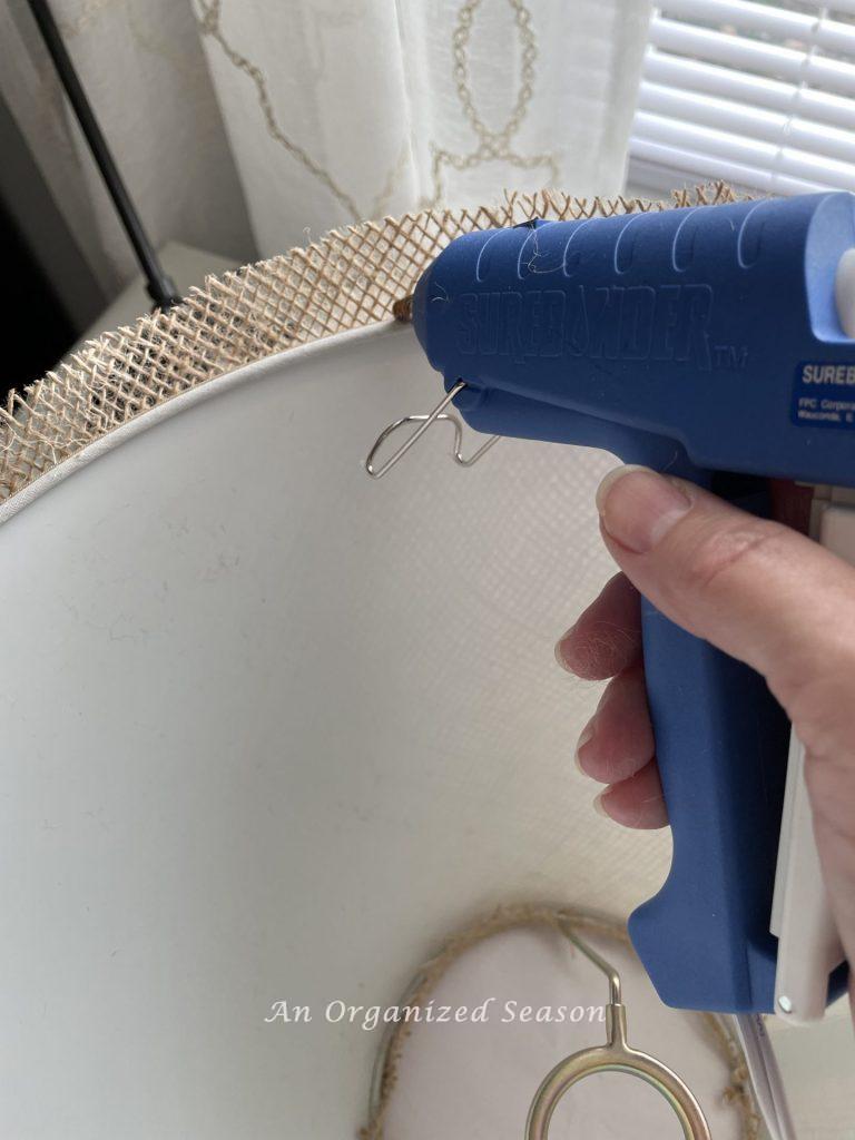 A glue gun applying hot glue to bottom edge of lamp. Showing step nine for how to makeover an old lamp to match new decor! 