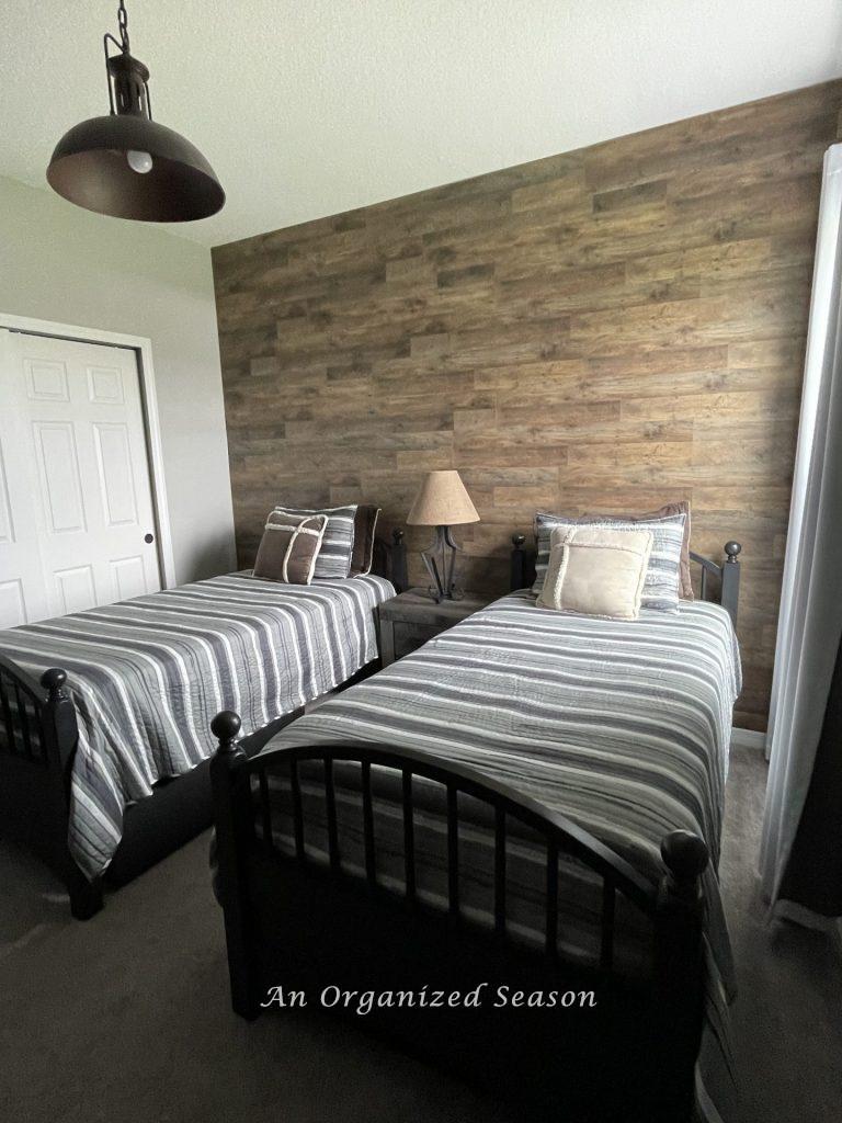 A bedroom with rustic wood flooring mounted on one wall.  Showing step three of how to makeover a bedroom into a rustic retreat.