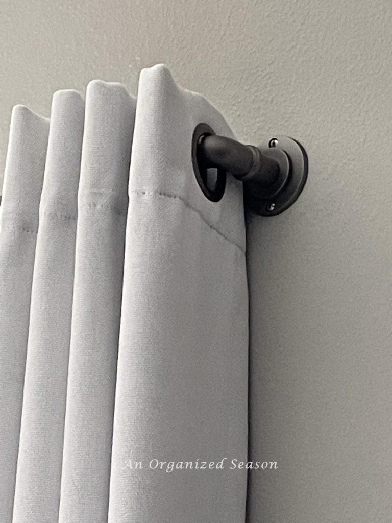 A rustic metal pipe used as a curtain rod holding a white curtain with grommets. Step one for how to makeover a bedroom into a rustic retreat.