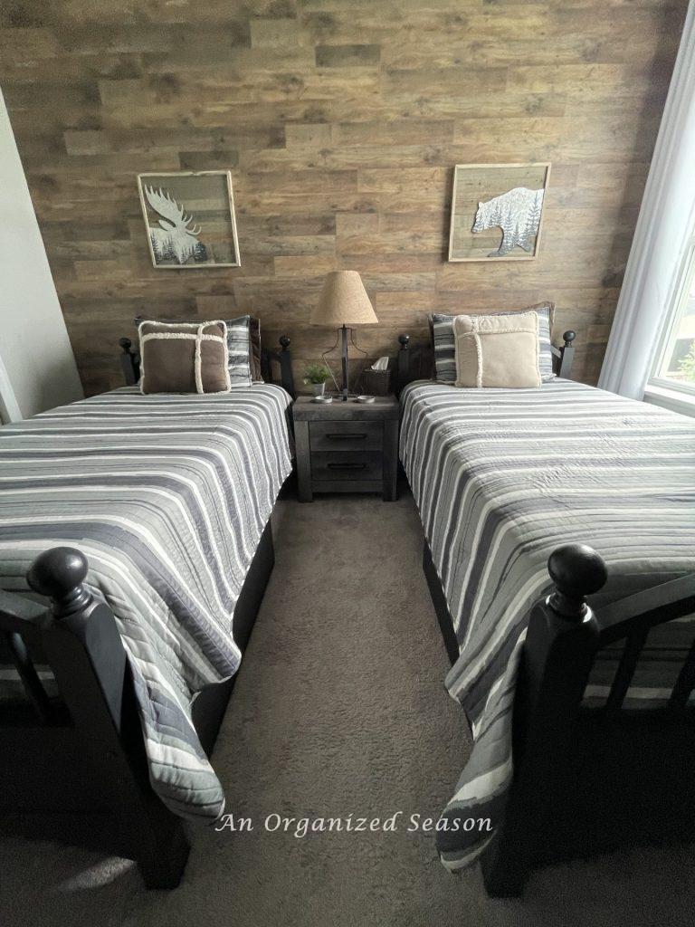 A bedroom with gray carpet that matches the rustic wood paneled wall. Showing step four for how to makeover a bedroom into a rustic retreat. 