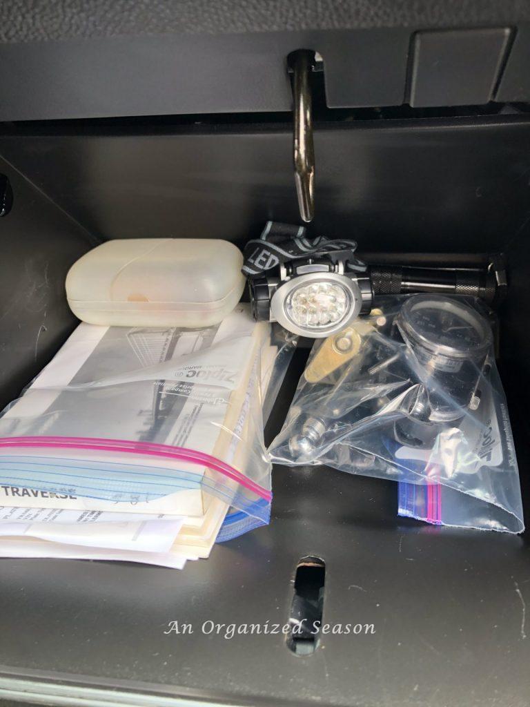 An organized glove compartment that has car manual and papers in a bag.  Camper equipment in a bag and first aid kit in a plastic travel soap dish. Tips to organize and clean your car.