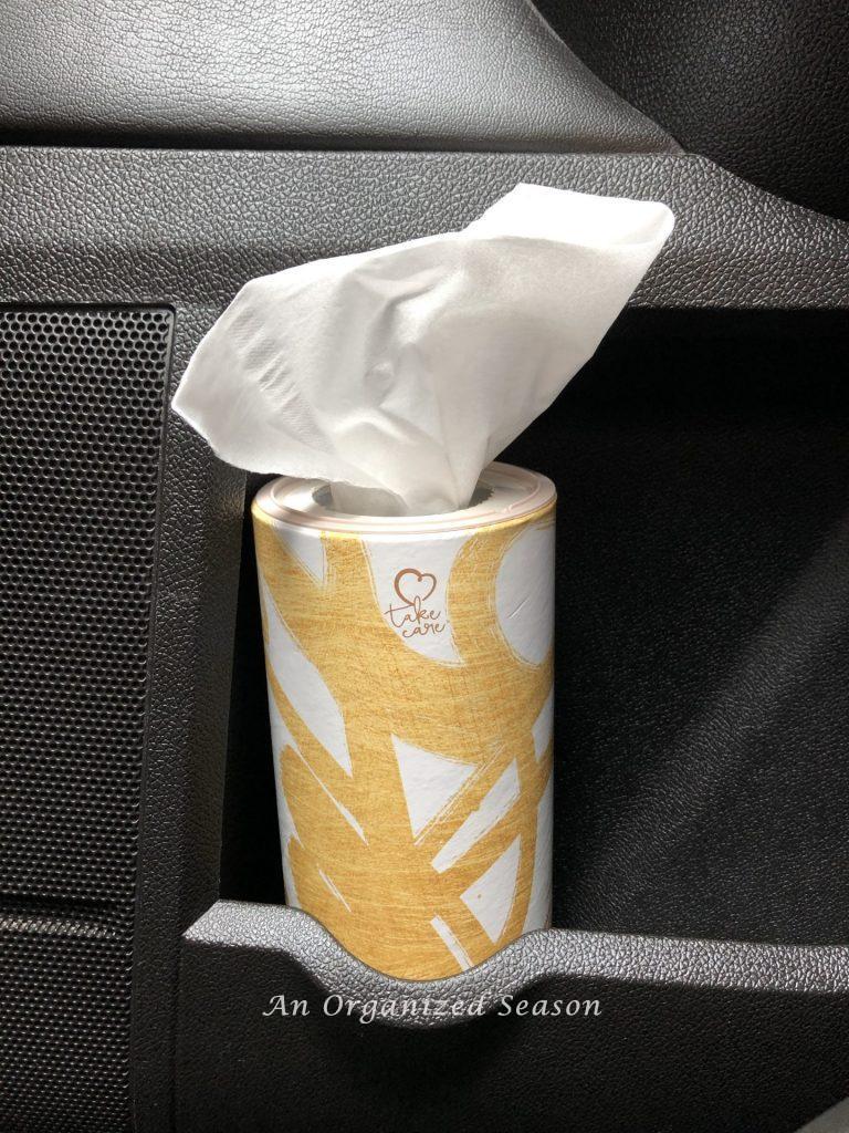 A round shaped tissue holder placed in the cup holder of a car door. An example of tips to organize and clean your car.