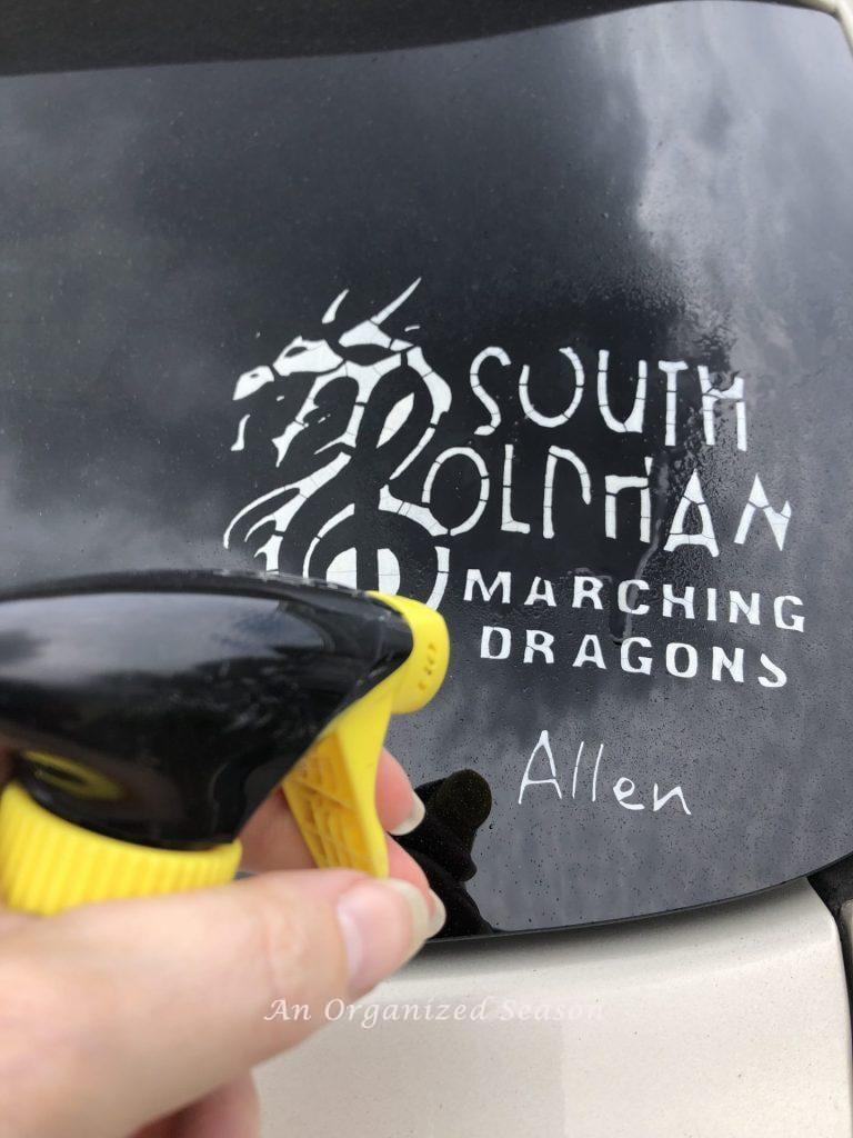 Someone spraying Goo Gone on a peeling window decal attached to a car window. Showing a tip to clean and organize your car.