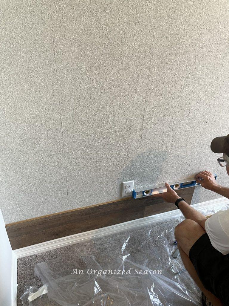 a man holding bubble level making sure row of flooring installed on wall is secure and level