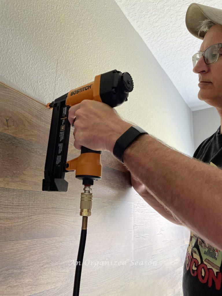 Man securing flooring boards to wall with brad nailer gun