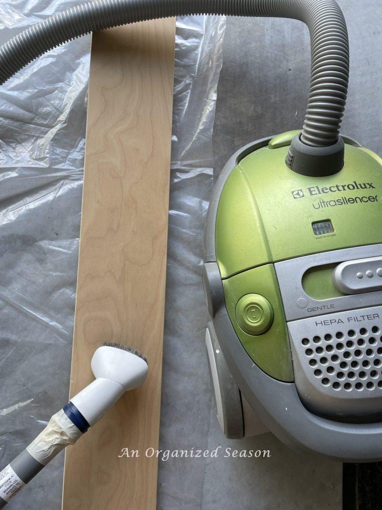 A vacuum sucking dust off  a twin bed side rail.  Showing step two for how to refinish twin beds with chalk paint.