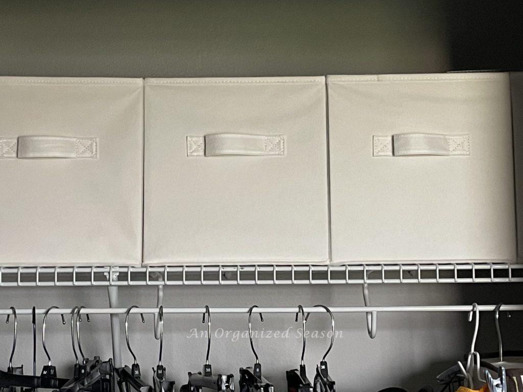 White fabric storage cubes on the top shelf of a closet. 