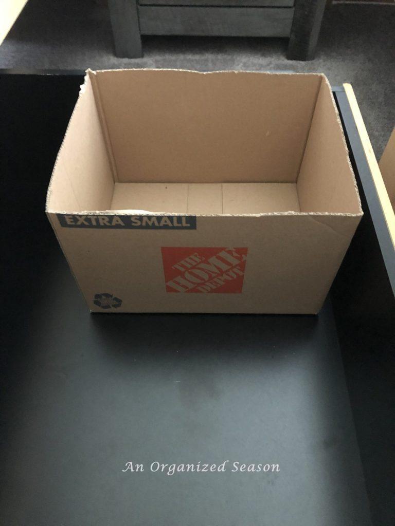 A small cardboard box with the top cut off, inside a storage drawer.